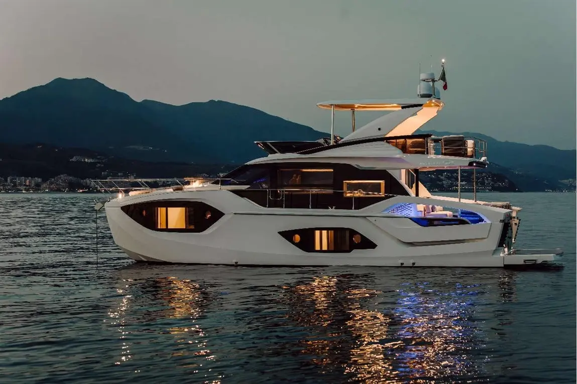 Luxury yacht moored at twilight, illuminated with blue lights, reflecting on calm waters and surrounded by mountains.
